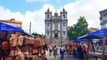 Marché de rue à Porto avec des sacs en cuir suspendus devant une église aux azulejos