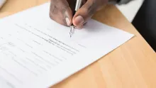 Main qui signe un contrat avec un stylo plume sur un bureau en bois clair