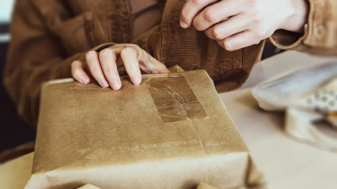 Mains qui scotchent un colis emballé dans du papier kraft
