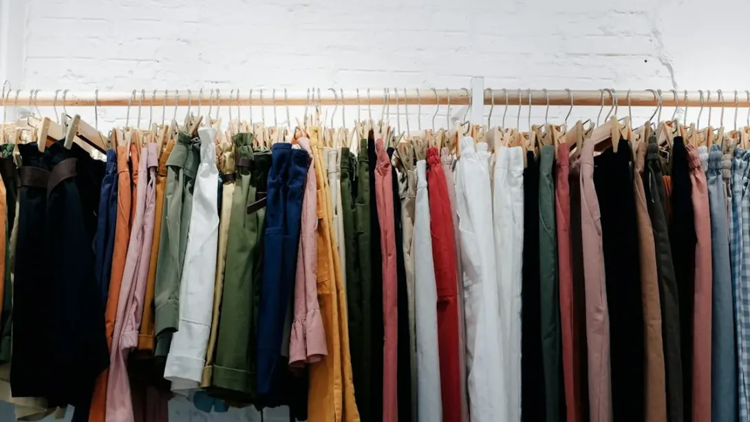 Longue tringle de vêtements colorés alignés sur des cintres devant un mur blanc
