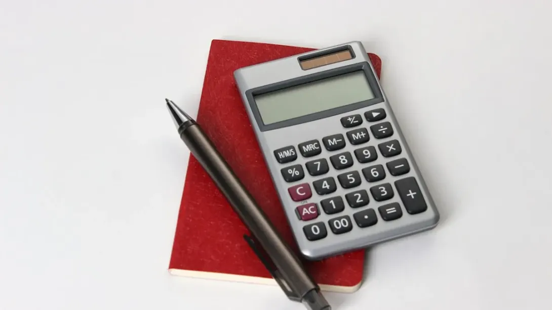 Calculatrice posée sur un carnet rouge avec un stylo, sur fond clair