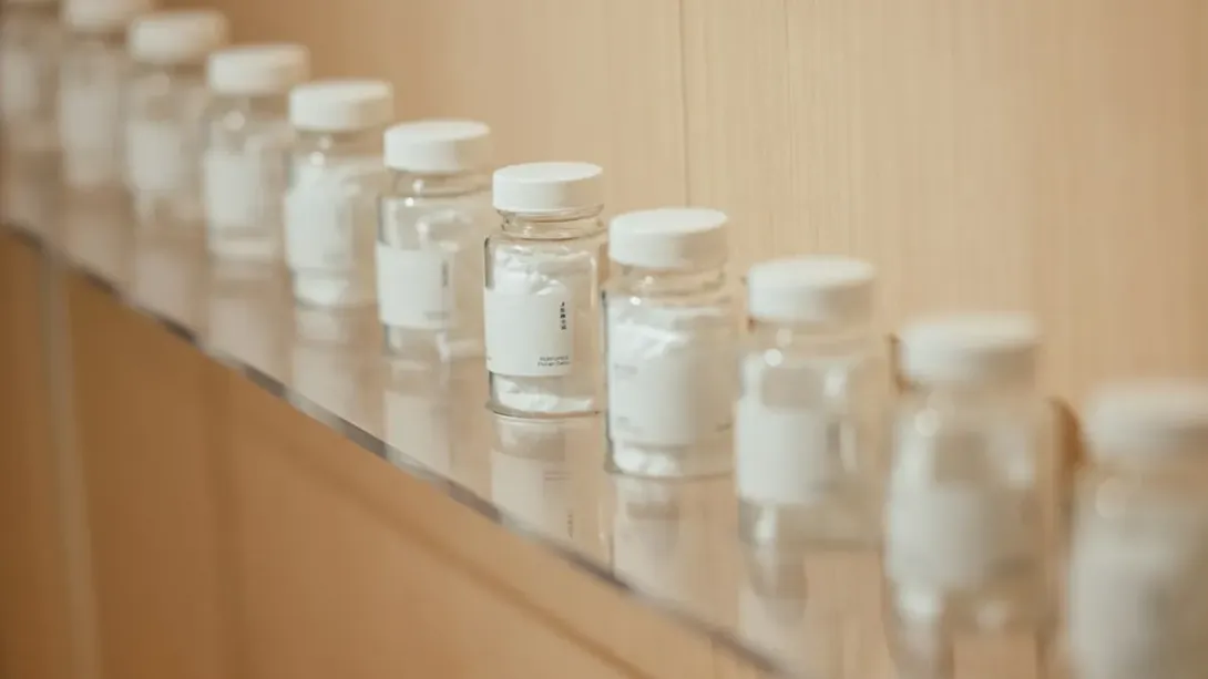 Rangée de petits flacons blancs à étiquette vierge alignés sur une étagère en bois