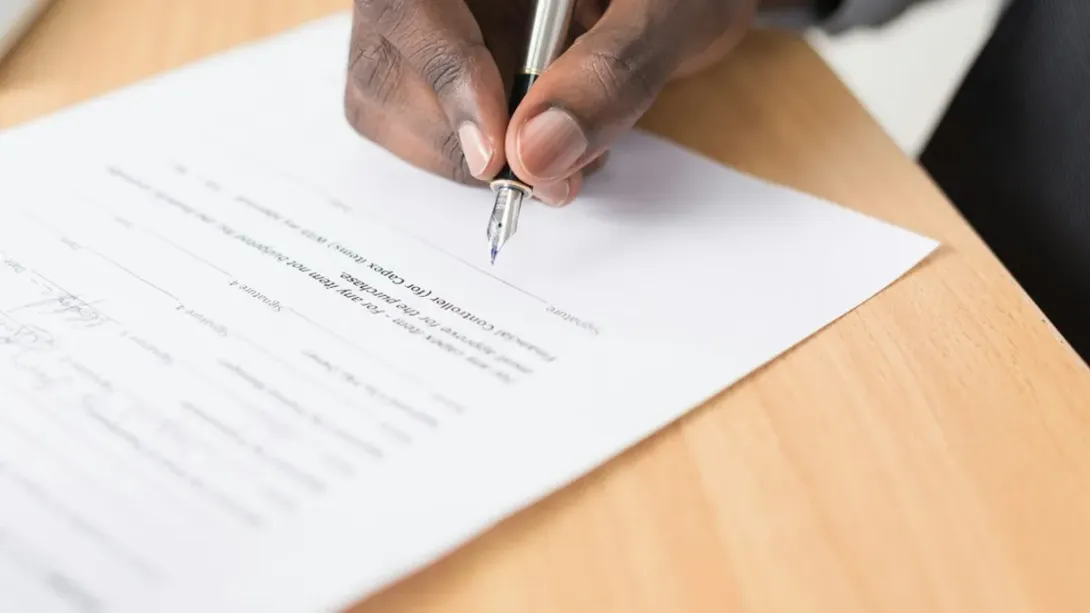 Main qui signe un contrat avec un stylo plume sur un bureau en bois clair